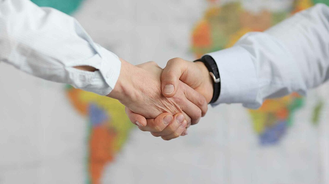Foto: zwei Menschen geben sich die Hand vor einer Weltkarte - Partnerstädte