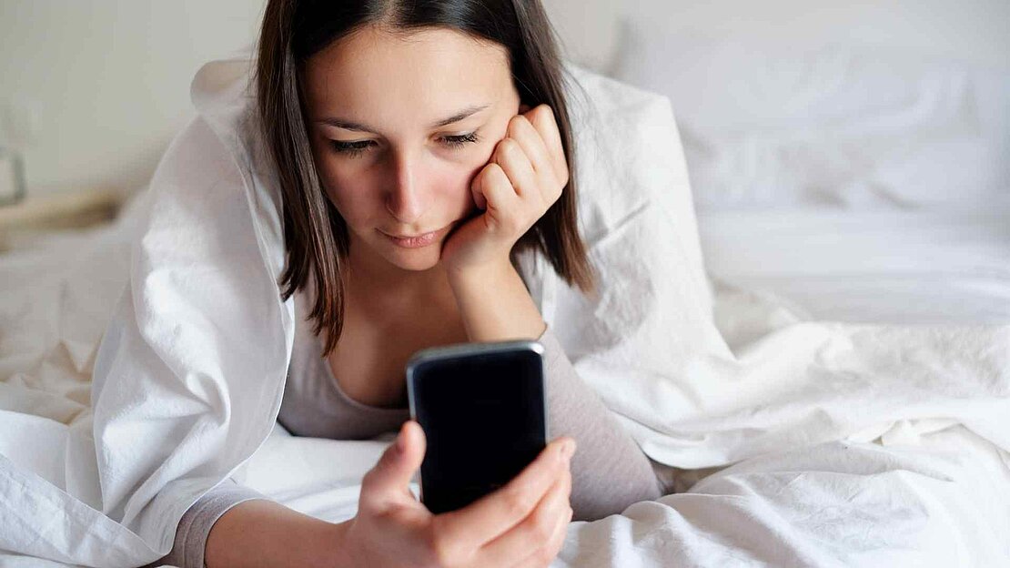 Foto: junge Frau die traurig auf ihr Smartphone schaut 