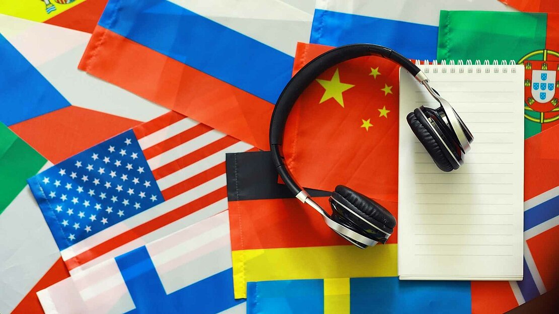 Foto: Kopfhörer und Block liegen auf Flaggen aus aller Welt - Sprachkurse