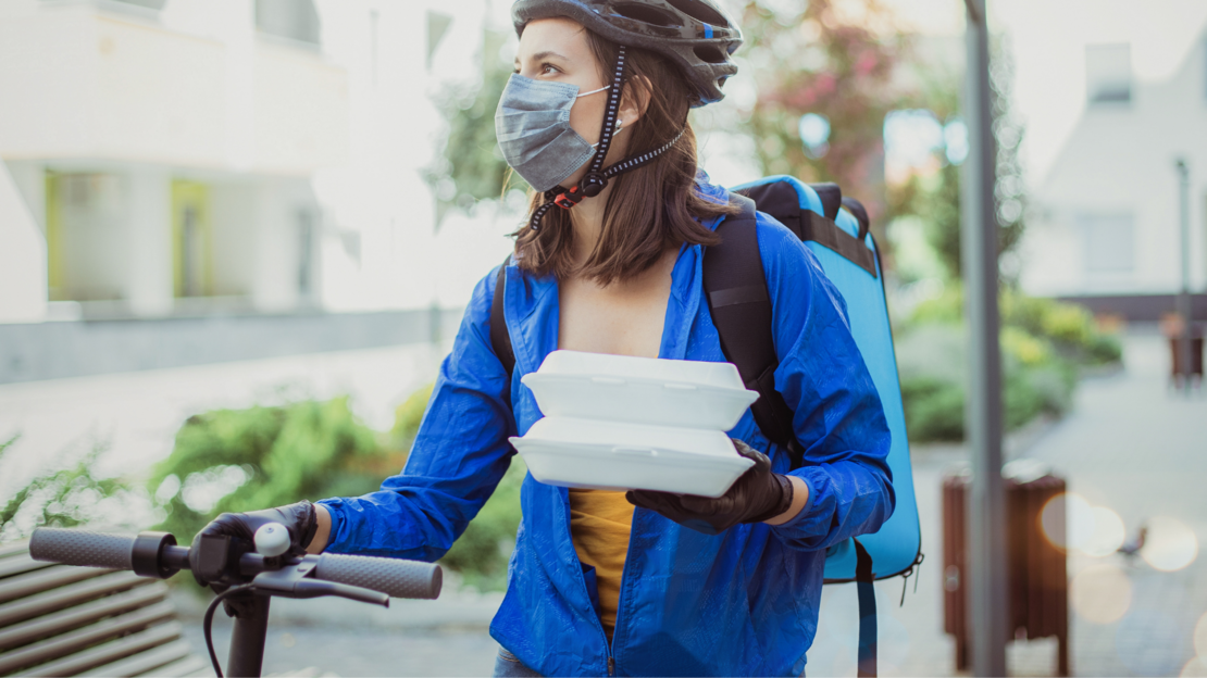 Foto: junge Frau mit Helm und eingepacktem Essen an ihrem Fahrrad